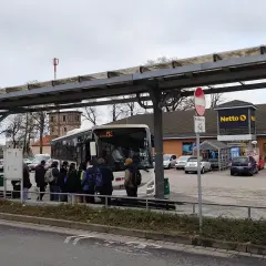 Ludzie czekają na autobus pod wiatą przystankową w Poznaniu Mielnie, obok sklepu Netto.