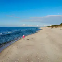 Samotna postać w różowym płaszczu spaceruje po plaży w Krynicy Morskiej. Wyobraź sobie, że to ostatni wagon pociągu do raju.
