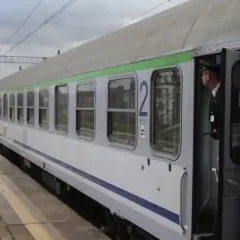 Konduktor w czapce stoi w otwartych drzwiach pociągu z zieloną górą, gotowy do odjazdu ze Szczecina.