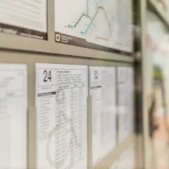 Rozkład jazdy autobusów Kraków. Widoczne tablice z godzinami odjazdów, mapka linii i ludzie czekający na przystanku.