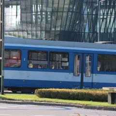 Niebieski tramwaj MPK Kraków stoi na tle nowoczesnego budynku. Sprawdź aktualny mpk kraków bilety cennik przed podróżą.