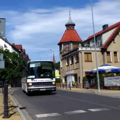 Autobus PKS w Międzyzdrojach zbliża się do dworca kolejowego. Słoneczny dzień, budynki z czerwonymi dachami.