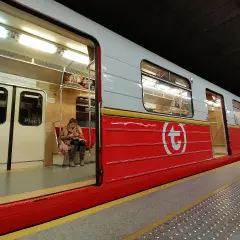 Kobieta czeka na swiateczne metro. Czerwony wagon z białym logo.