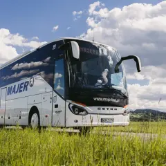 Autobus Majer na trasie Kraków - Mszana Dolna jedzie przez zielone pola pod błękitnym niebem.