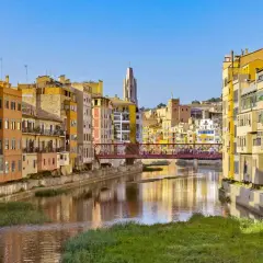 Kolorowe kamienice nad rzeką w Gironie, z mostem łączącym z Barceloną w tle.