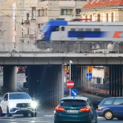Pędzący pociąg IC 407 na trasie Chopin mija ruchliwe skrzyżowanie z samochodami i tramwajami w tle.