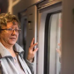 Starsza pani w okularach podróżuje pociągiem, ciesząc się zniżkami dla emerytów.