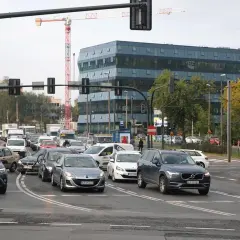Kraków, rondo matecznego w godzinach szczytu. Samochody stoją w korku, w tle nowoczesny budynek i dźwig budowlany.