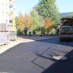 Prace drogowe na osiedlu Zygmunta Augusta w Limanowej. Walec drogowy ubija asfalt, a pracownicy układają kostkę.