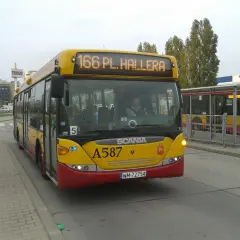Żółty autobus linii 166 w Warszawie, z numerem bocznym A587, zbliża się do przystanku obok centrum handlowego Tesco.