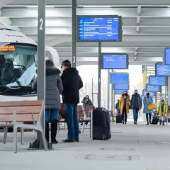 Na dworcu w Katowicach, przy tablicy z odjazdami, ludzie czekają na autobusy. Sprawdź rozkład, by dowiedzieć się, jak dojechać z dworca w Katowicach na Medyków.