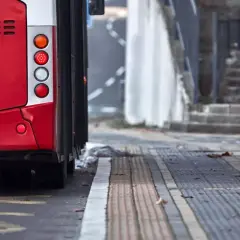 Czerwony autobus 74 stoi na przystanku. Widać jego tylne światła i część karoserii.