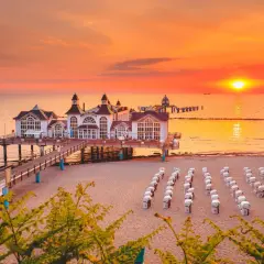 Zachód słońca nad Rugią, idealny cel podróży z Polski. Molo z białymi budynkami, plaża z rzędami koszy plażowych.