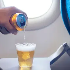 Ręka z puszką piwa nalewa napój do szklanki na stoliku w samolocie. Czy można przewozić alkohol samolotem?