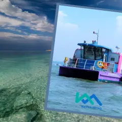 Kolorowa łódź "Water Metro" płynie po spokojnej, turkusowej wodzie. W tle widać skaliste wybrzeże i błękitne niebo z chmurami.