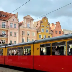 Czerwono-żółty tramwaj z numerem 87 jedzie ulicą Grudziądza. W tle kolorowe kamienice.