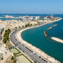 Widok na port w Bari, gdzie statki i dźwigi tworzą tło dla miejskiej komunikacji.