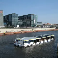 Statek wycieczkowy płynie wzdłuż Sprewy obok nowoczesnych budynków Berlin Hauptbahnhof, gdzie znajdują się perony.