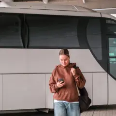 Młoda kobieta z telefonem czeka na autobus, który ma awarię taboru.