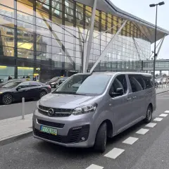 Srebrny bus czeka na pasażerów przed nowoczesnym terminalem lotniska. Może to być transport z Koszalina do Gdańska na lotnisko.