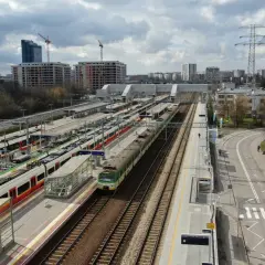 Dworzec Gdański w Warszawie z wieloma pociągami na torach i nowoczesnymi budynkami w tle.