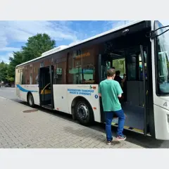 Biały autobus miejski z otwartymi drzwiami, wsiada pasażer.