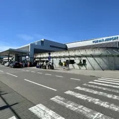 Lotnisko Poznań Airport, z ludźmi i samochodami przed budynkiem. Tu znajdziesz informacje, jak dojechać z dworca PKP na lotnisko w Poznaniu.