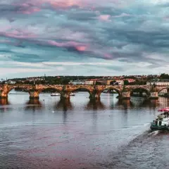 Zachód słońca nad Pragą, idealny na wycieczki jednodniowe z Jeleniej Góry. Widok na Most Karola i rzekę Wełtawę z łodzią.
