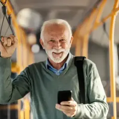 Uśmiechnięty starszy pan z telefonem w dłoni, trzymający się poręczy w pojeździe. Cieszy się z możliwości 70 lat darmowe przejazdy PKP Intercity.