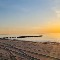 Zachód słońca nad morzem, piaszczysta plaża z widocznymi śladami opon, falochrony. Idealne miejsce na odpoczynek po podróży, nawet jeśli wicie dojazd PKP.