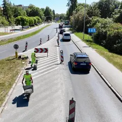 Prace drogowe na linii 101 Szczecin. Robotnicy w kamizelkach odblaskowych przygotowują nawierzchnię, jeden z nich pcha taczkę z materiałem.