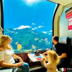 Rodzina podziwia alpejskie widoki przez okno pociągu Bernina Express. Bilety na tę podróż to gwarancja niezapomnianych wrażeń.