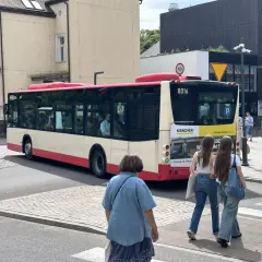 Autobus linii 148 w Gdańsku, z numerem bocznym 8016, odjeżdża z przystanku. Na pierwszym planie dwie dziewczyny idące przez pasy.
