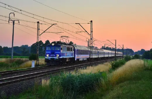 Niebieski pociąg PKP EP07-389 z wagonami mija pole o zachodzie słońca, jadąc w stronę Kołobrzegu.
