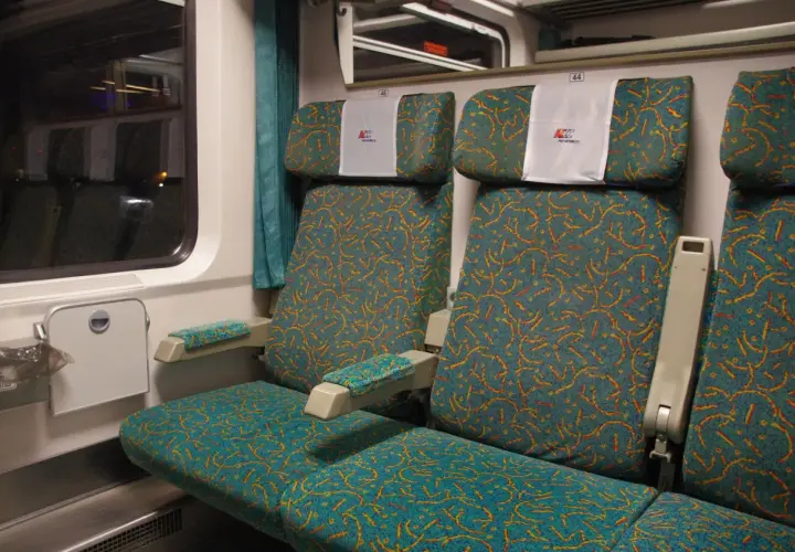 Wnętrze wagonu PKP Intercity. Widok na dwa rzędy siedzeń z charakterystycznym wzorem. Wybór miejsca ze schematu jest kluczowy dla komfortowej podróży.