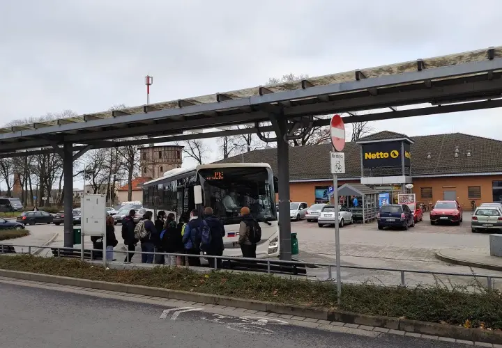 Ludzie czekają na autobus pod wiatą przystankową w Poznaniu Mielnie, obok sklepu Netto.
