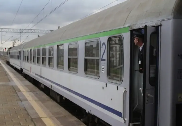 Konduktor w czapce stoi w otwartych drzwiach pociągu z zieloną górą, gotowy do odjazdu ze Szczecina.