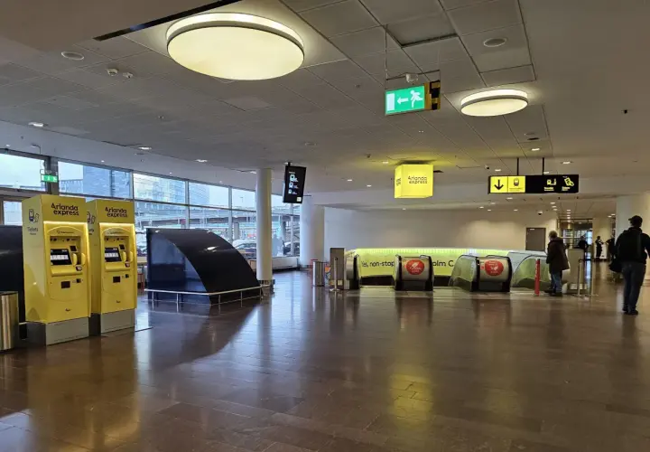 Żółte automaty biletowe Arlanda Express i schody ruchome prowadzące do pociągu.