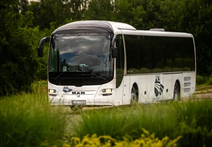 Biały autokar PKS z Jarosławia jedzie przez zielony, bujny krajobraz.