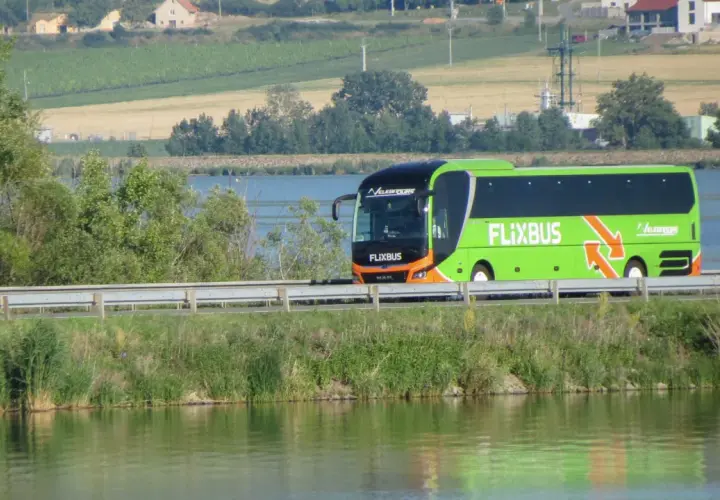 Zielony autobus Flixbus jedzie wzdłuż jeziora. Szukaj flixbus promocje na podróż!