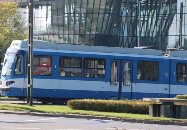 Niebieski tramwaj MPK Kraków stoi na tle nowoczesnego budynku. Sprawdź aktualny mpk kraków bilety cennik przed podróżą.