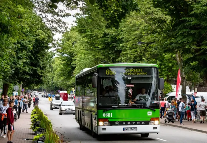 Zielony autobus linii 666 jedzie w kierunku Karwii i Jastrzębiej Góry. Na poboczu spacerują ludzie, ciesząc się letnim dniem.