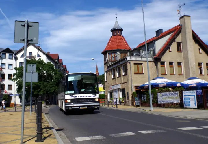Autobus PKS w Międzyzdrojach zbliża się do dworca kolejowego. Słoneczny dzień, budynki z czerwonymi dachami.