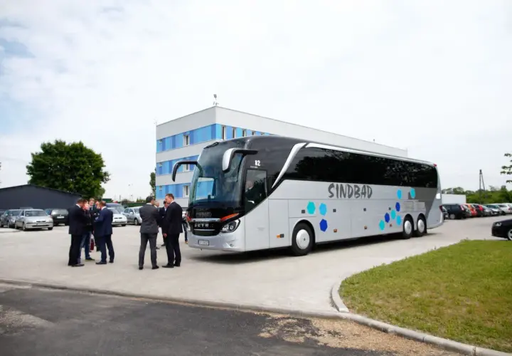 Grupa mężczyzn w garniturach rozmawia przy autokarze Sindbad. Sprawdzają ceny biletów przed podróżą.