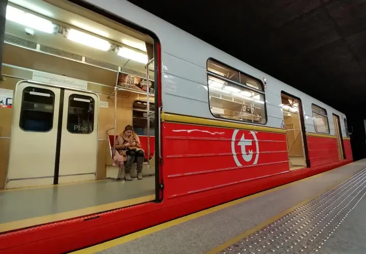 Kobieta czeka na swiateczne metro. Czerwony wagon z białym logo.