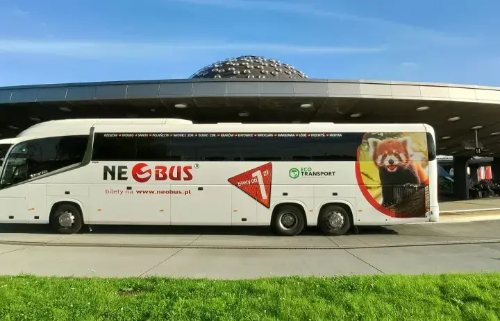 Biały autokar Neobus z pandą małą na boku stoi pod nowoczesnym zadaszeniem. Sprawdź neobus ceny biletów na www.neobus.pl.