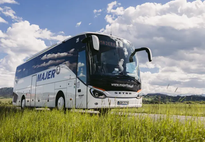 Autobus Majer na trasie Kraków - Mszana Dolna jedzie przez zielone pola pod błękitnym niebem.