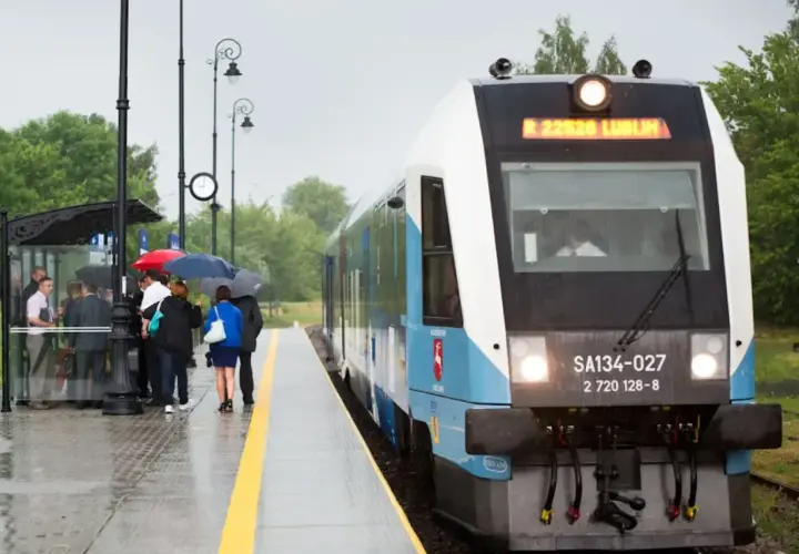 Pasażerowie z parasolami czekają na peronie na pociąg Kolei Lubelskich.