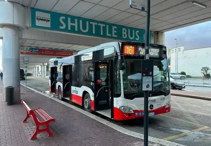 Autobus wahadłowy na lotnisku Bari czeka na pasażerów pod zielonym znakiem "SHUTTLE BUS".