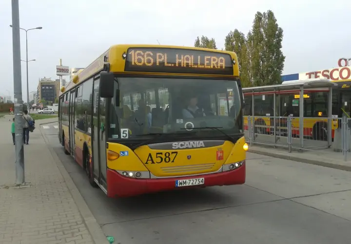 Żółty autobus linii 166 w Warszawie, z numerem bocznym A587, zbliża się do przystanku obok centrum handlowego Tesco.